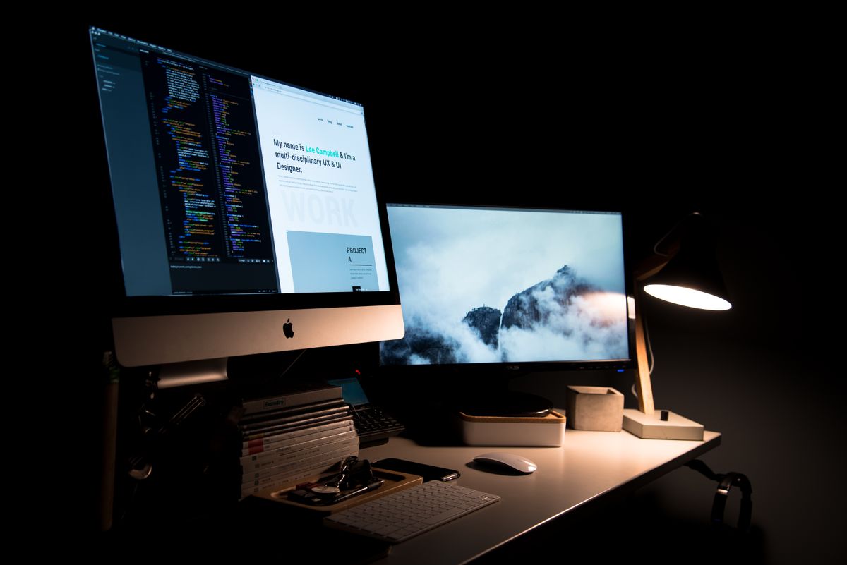 A dark studio desk — code on one screen, work in progress on the other